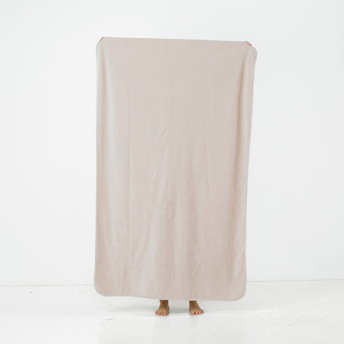 Someone stands behind the Splash Blanket The OG Waterproof Blanket - Medium in light beige, holding it up with only their bare feet visible below, set against a white background.