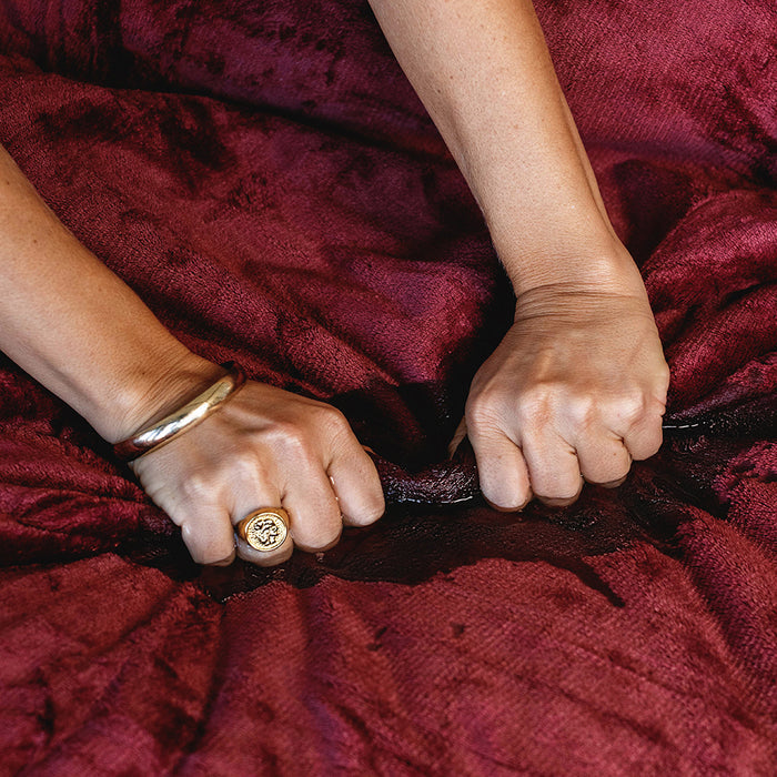 Two hands grip and bunch up the Splash Blanket The OG Waterproof Blanket - Medium in dark red. One hand wears a gold ring and bracelet. The waterproof, textured fabric beneath the hands looks wet and wrinkled.