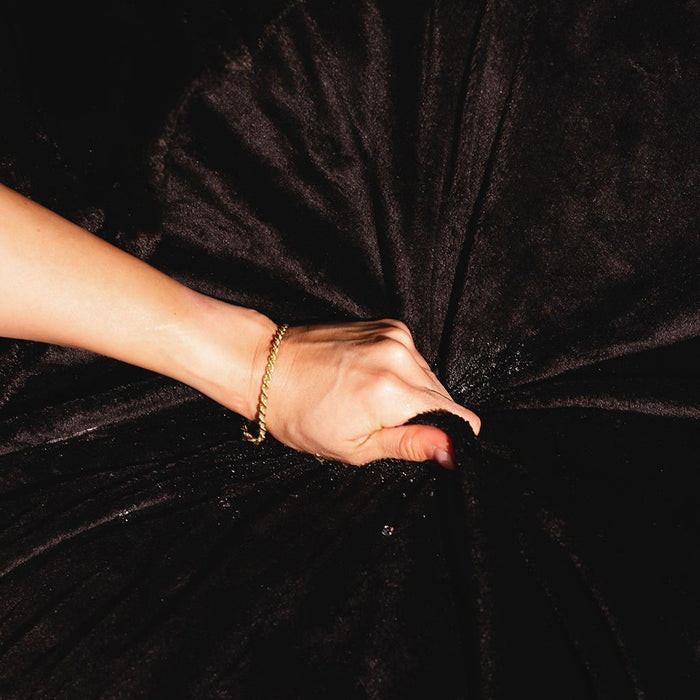 A hand grips and bunches up the Splash Blanket Furlush Luxurious Faux Fur Waterproof Blanket - Small in soft black, showing its rich plush texture with deep folds and shadows.