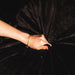 A hand grips and bunches up the Splash Blanket Furlush Luxurious Faux Fur Waterproof Blanket - Small in soft black, showing its rich plush texture with deep folds and shadows.