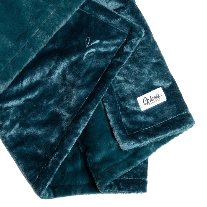 A close-up of the Splash Blanket The OG Waterproof Blanket - Small in soft teal micro-velvet, featuring a stitched leaf design, white "Splush" tag, velvety texture, spill-proof surface, and neatly folded presentation.