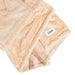A neatly folded Splash Blanket Furlush Luxurious Faux Fur Waterproof Blanket - Medium in light beige is shown, featuring a stitched white Splash Home logo label and an embroidered corner design.