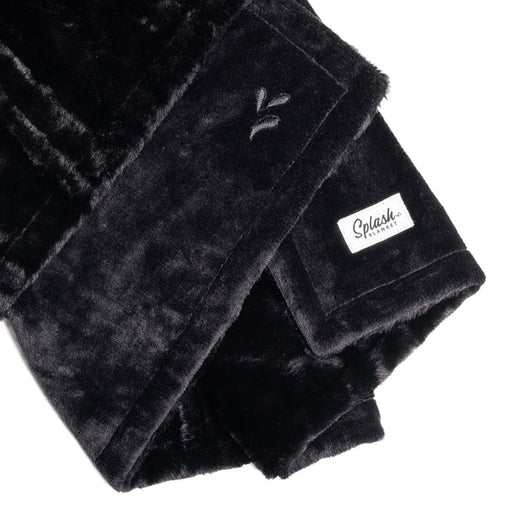 A close-up of the Splash Blanket Furlush Luxurious Faux Fur Waterproof Blanket in black velvet shows an embroidered leaf design and a white rectangular "Splash" tag on the corner.