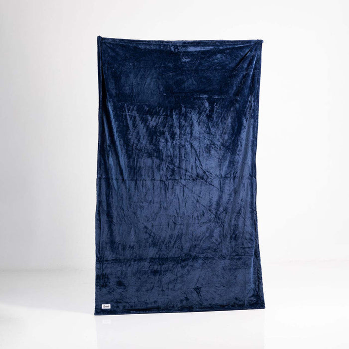 The Splash Blanket Furlush Luxurious Faux Fur Waterproof Blanket - Large in dark blue velvet hangs vertically against a plain white background, showcasing its plush, soft texture and a small white tag in the bottom left corner.