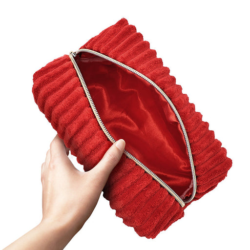 A hand holds the Plush Zip Up Toy Storage Bag, featuring red textured fabric and a gold zipper, partially open to show its smooth, shiny red lining inside.