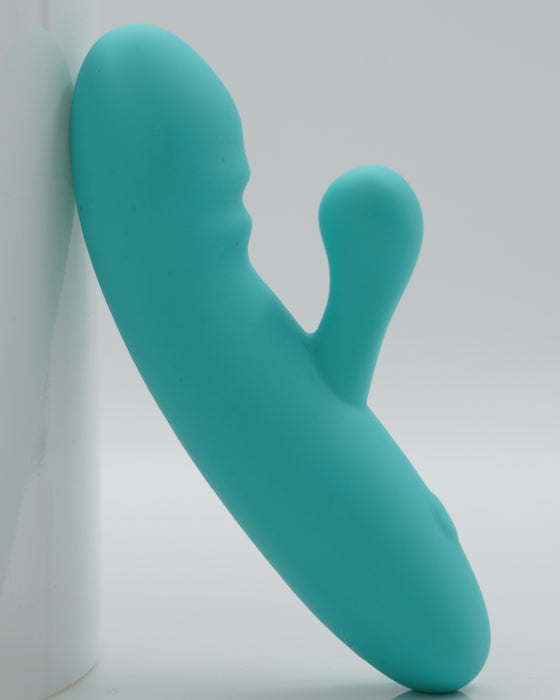 A turquoise Creative Conceptions Rabbit Ultra Soft First Time Flexible Silicone Vibrator, featuring a dual-ended design for g-spot and clitoral stimulation, leaning against a white backdrop.