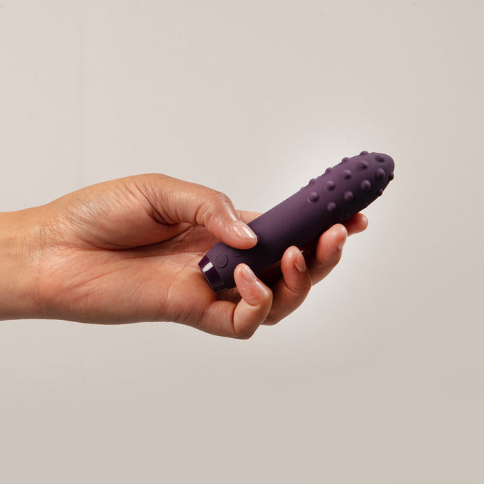 Hand holding a deep purple silicone bullet vibrator with textured nubs.
