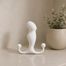 The Aneros Original Progasm Hands-Free Prostate Massager (Large), a white, curved silicone device with two rounded ends, stands upright on a beige countertop beside a green potted plant, ready for hands-free prostate stimulation.
