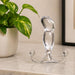 The Aneros Progasm Ice Hands-Free Prostate Massager (Large), made of clear glass with a curved, bulbous shape and two round ends, rests on a marble countertop beside a green potted plant, ready for hands-free use.