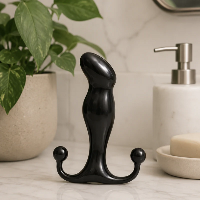 A black Aneros Progasm Jr. Hands-Free Prostate Massager stands upright on a marble bathroom countertop next to a potted plant, soap dispenser, and bar of soap—ideal for hands-free prostate stimulation.