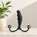 The Aneros Psy Adjustable Prostate Massager, a black textured stimulator with dual round handles, stands upright on a marble surface. A green potted plant is in the background, and bright lighting highlights its hands-free design.