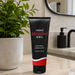 A black tube of Aneros Sessions Water Based Gel Lubricant (4.2 oz) sits on a bathroom counter near a green potted plant and soap dispenser, with a mirror behind—ideal for enhancing anal play or using with prostate massagers.