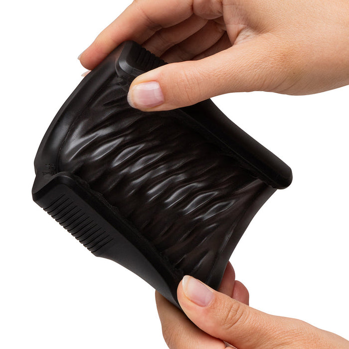 Two hands hold and squeeze the Arcwave Zing Adjustable Vibrating Silicone Masturbator, a sleek black male stroker featuring textured ridges and grooves for flexible stimulation.