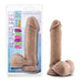 The Au Naturel Long 8 Inch Dual Density Medium Tone Suction Cup Dildo with Balls stands upright by its clear packaging, which features colorful labels highlighting its soft, firm, flexible texture, strap-on compatibility, and Sensa Feel material.