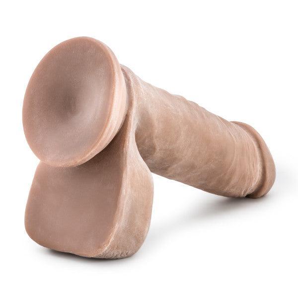 The Au Naturel Long 8 Inch Dual Density Medium Tone Suction Cup Dildo with Balls is a realistic, flesh-toned silicone toy featuring a testicle-shaped base; it's strap-on compatible for versatile play and shown lying on its side against a white background.