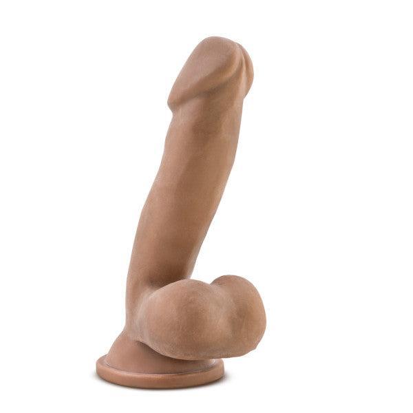The image shows the Au Naturel 6.5 Inch Dual Density Suction Cup Dildo - Mocha by Blush, a realistic brown silicone dildo with an upward curved shape, featuring a detailed head and base, perfect for targeting the g-spot or prostate.
