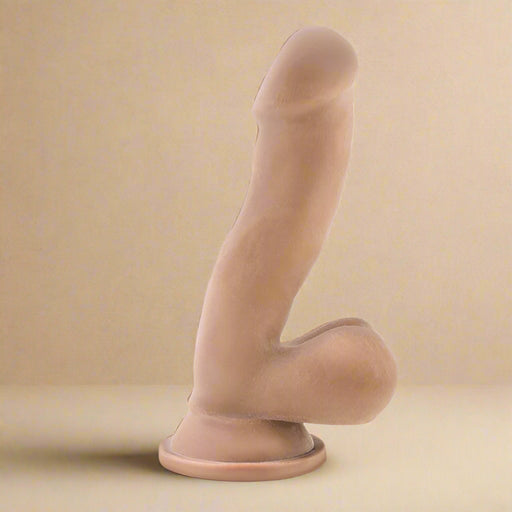 The Blush Au Naturel 6.5 Inch Dual Density Suction Cup Dildo in Mocha is a realistic flesh-colored dildo featuring a prominent head, textured shaft, and attached testicles. The base has a suction cup for hands-free use or compatibility with a strap-on harness. Crafted using Dual Density Sensa Feel for an authentic experience, its shape closely mimics a natural human penis.