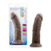 The Au Naturel Thick 8 Inch Realistic Feel Dual Density Dark Tone Suction Cup Dildo is displayed beside its packaging, showcasing its harness compatibility and soft yet firm, flexible material.