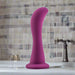 The Bellatrix Slim Curved 6.25 Inch Purple G-Spot and Prostate Dildo with Suction Cup stands upright on a bathroom sink, with a tiled wall and faucet visible in the background.