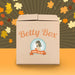 A cardboard box from Betty's Toy Box with the words "Betty Box" printed on it, featuring a vintage-style image of a woman below, labeled "Betty's Cliterrific Mystery Box - Fall/Winter Edition" on an orange ribbon. The background has a gradient of brown and yellow with scattered autumn leaves.