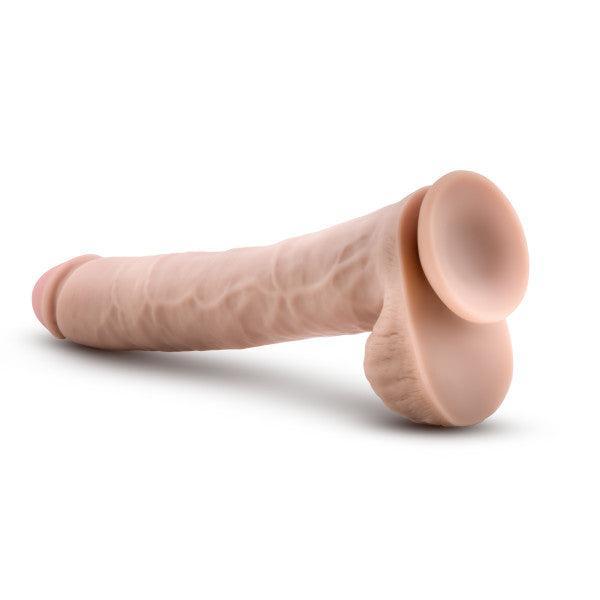 The Big Daddy 14 Inch Dual Density Suction Cup Dildo - Vanilla by Blush is a realistic, flesh-colored dildo that mimics the appearance and feel of a human penis with its veined texture and strong suction cup base. The toy is displayed lying on a white surface.