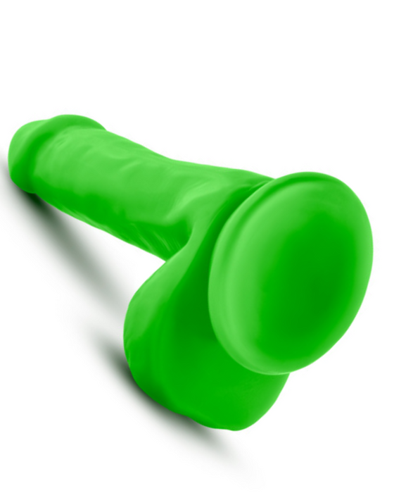 The Neo Elite Beginner 6 Inch Silicone Dual Density Dildo with Balls, a bright green phallic toy featuring a flared base, rests on a white surface.