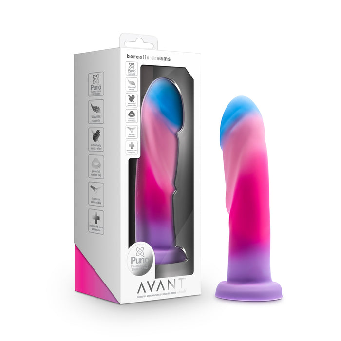 The Borealis Dreams Girthy Textured 7.75 Inch Silicone Dildo, with a pink, purple, and blue gradient, stands beside its Avant packaging. This silicone dildo features a suction cup base and is harness compatible for versatile pleasure.