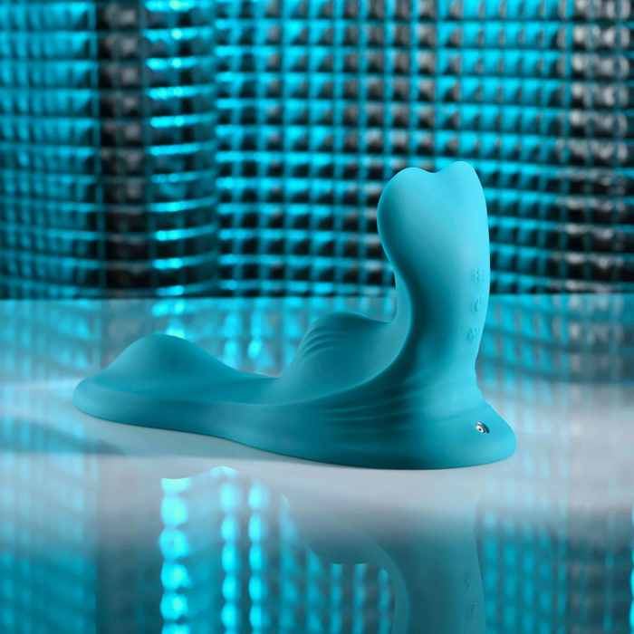 The Bumps & Grind Triple Bump Flexible Grinding Vibrator, a blue silicone adult toy with a curved design and flexible pleasure pad, is displayed on a reflective surface against a textured, blue-lit background.