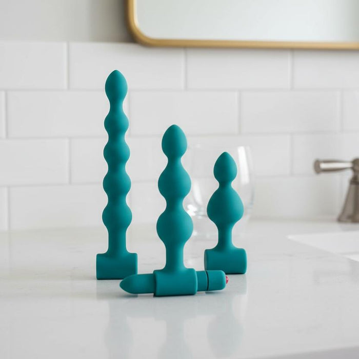 The Bumpy 3-Piece Beaded Anal Plug Set with Vibrating Bullet includes three teal beaded plugs of various sizes and shapes, each displayed upright, with one plug featuring a removable vibrating bullet for customizable pleasure.