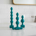The Bumpy 3-Piece Beaded Anal Plug Set with Vibrating Bullet includes three teal beaded plugs of various sizes and shapes, each displayed upright, with one plug featuring a removable vibrating bullet for customizable pleasure.