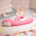 The Bunny Kisses Rechargeable Silicone Rabbit Vibrator in pink rests on a marble surface with rose petals, folded white towels, and a glass plate in the background.
