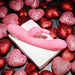The Bunny Kisses Rechargeable Silicone Rabbit Vibrator in pink rests on a white box, surrounded by glittery red and pink heart-shaped decorations—ideal for clitoral stimulation.