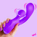 A hand with purple painted nails holds the Clit Tapping G-Spot Pulsing Rabbit Flexible Silicone Vibrator against a pastel purple background, with illustrated vibration lines showing its stimulation. The word "BANG!" appears in the corner.