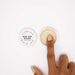 A hand with manicured nails dips a finger into an open jar of Clitherapy Bad Day Killer Clitoral Balm - Star Anise Scent, known for its warming effect. The lid is nearby on a clean white surface.