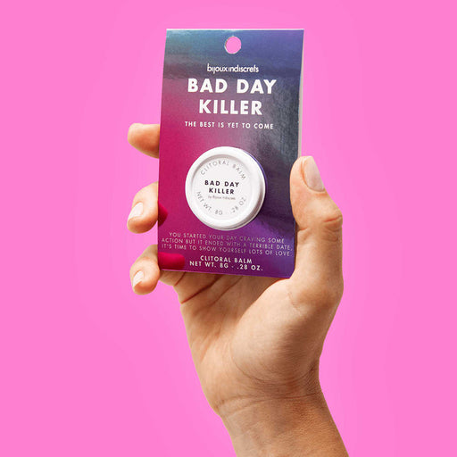 A hand holds a packaged tin labeled "Clitherapy Bad Day Killer Clitoral Balm - Star Anise Scent" by Bijoux Indiscrets against a pink background, with text highlighting sensitivity boosting effects and the phrase "The best is yet to come.