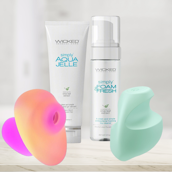 Two tubes of Wicked Sensual Care stand behind the Clitoral Thrills Beginner's Bundle—featuring a pink and orange finger vibrator and a mint green clitoral stimulator—set against a soft, blurred background.