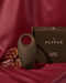 A couple's Pepper Connect Vibrating Cock Ring, presented on a luxurious maroon fabric background alongside an exotic leaf and elegant packaging.