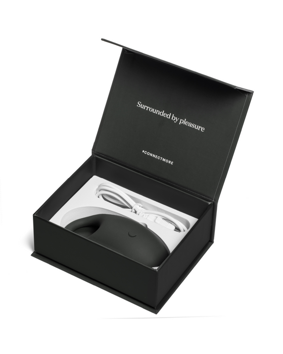 Elegant black packaging box opened to reveal a modern Pepper Connect vibrating cock ring, with the phrase "surrounded by pleasure" inscribed inside the lid, suggesting a premium unboxing experience.