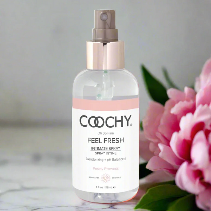 A clear Coochy Intimate Feminine Spray - Peony Prowess 4 oz sits beside a pink peony on a light surface, showcasing its pH-balanced feminine deodorant formula against a softly blurred background.