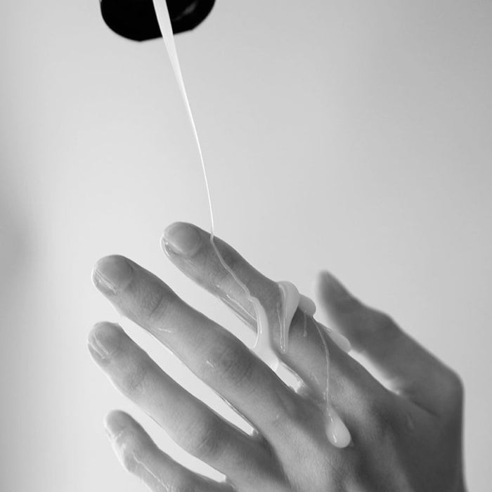 A hand is shown with Creamy Glide Milky Semen-Style Cum Lubricant (8.5 fl oz), white liquid poured over the fingers against a plain background.