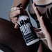Dressed in sheer black, a person dispenses Creamy Glide Milky Semen-Style Cum Lubricant (8.5 fl oz), a silky water-based gel, from its pump bottle, holding it between their hand and thigh.