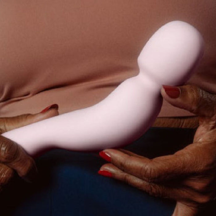 A person with red-painted nails holds the Dame Com Ergonomic Waterproof Wand Vibrator with Flexible Neck against their torso, highlighting its use for clitoral pleasure and personal self-care.