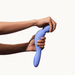 A person bends the Dame Com Ergonomic Waterproof Wand Vibrator, featuring a flexible neck and curved shape, with both hands against a plain white background.