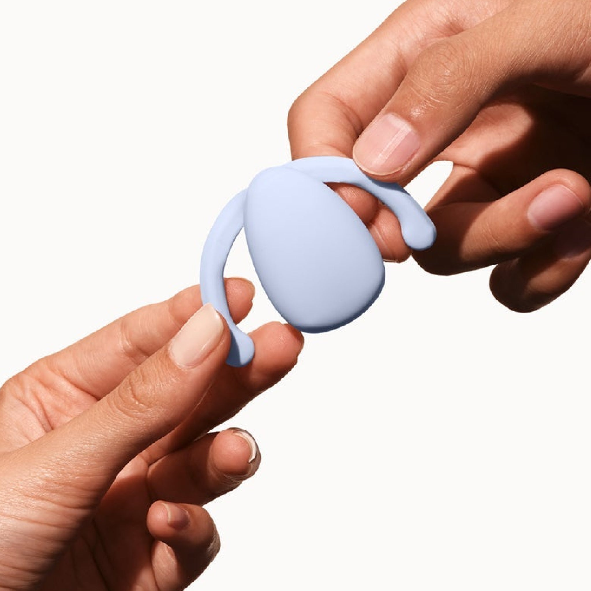 Hands holding an ice blue, silicone Dame Eva hands-free clitoral vibrator with flexible wings for a secure fit.
