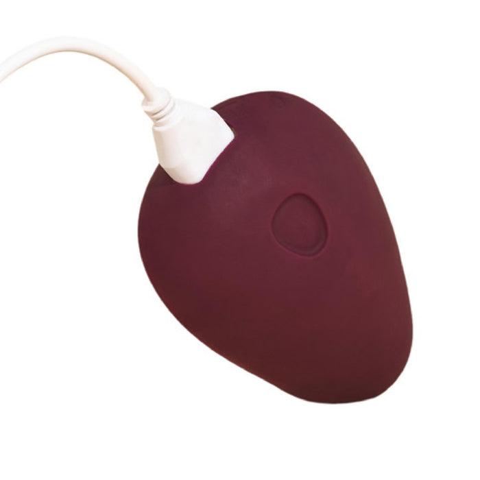 The Dame Pom Hand Held Flexible Vibrator in Plum is a maroon, heart-shaped device made from medical grade silicone with a white cord and an indented button on its surface.