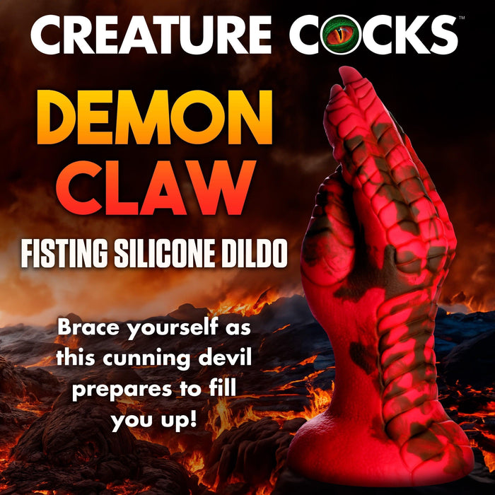 A red and black silicone sex toy shaped like a demon’s claw stands upright against a fiery volcanic backdrop. Bold text announces the "Demon Claw Long Thick Fantasy Fisting Silicone Dildo" by Creature Cocks.