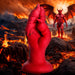 The Demon Claw Long Thick Fantasy Fisting Silicone Dildo stands tall on rocky ground surrounded by lava, with a muscular, winged demon looming in the fiery volcanic landscape behind.