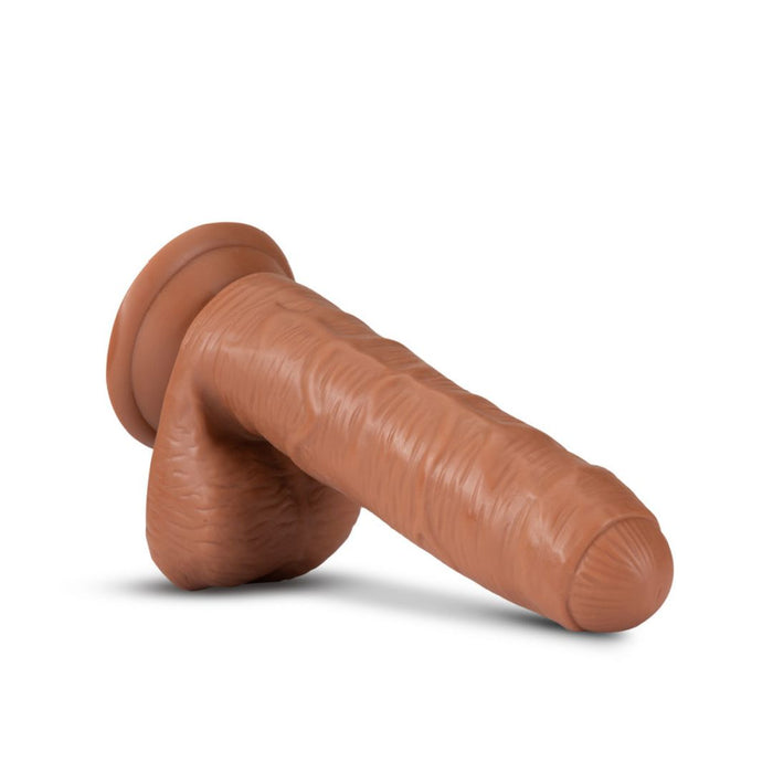 The Derek the Bartender Lifelike Uncut 7 Inch Medium Tone Dildo features realistic veins, a detailed scrotum, and a sturdy suction cup base. Displayed on a white background.