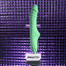 The Full Throttle Warming Waterproof Silicone Vibrator, in green with a ribbed shaft, sits on a clear stand labeled "EVOLVED" against a reflective purple tiled background under dramatic lighting.