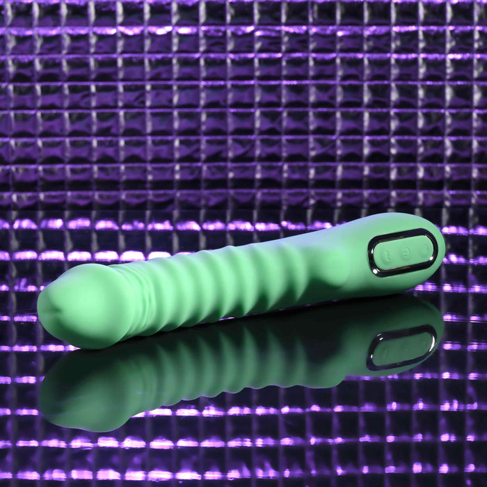 The Full Throttle Warming Waterproof Silicone Vibrator, featuring a ribbed green shaft and control buttons, rests on a reflective surface against a purple textured background.